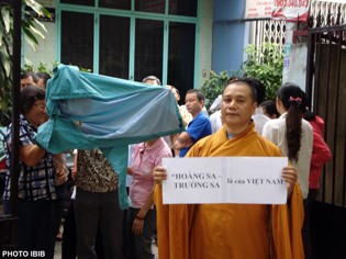Venerable Thich Vien Hy holds a poster: “The Paracel and Spratly islands belong to Vietnam”. Behind him, plain clothed Security agents hide their faces to avoid being recognized by demonstrators on the streets (Photo IBIB)